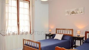 A bedroom with two wooden beds, a nightstand, a lamp, and a wall-mounted shelf with decorative items. - Quiet cottage near Azay-le-Rideau Castle (Azay-le-Rideau)