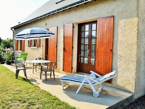 A house with a patio area featuring a table, chairs, and a sun lounger.