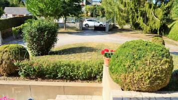 A residential driveway with a white car parked in the background, surrounded by well-maintained hedges and trees.