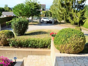 A residential driveway with a white car parked in the background, surrounded by well-maintained hedges and trees.