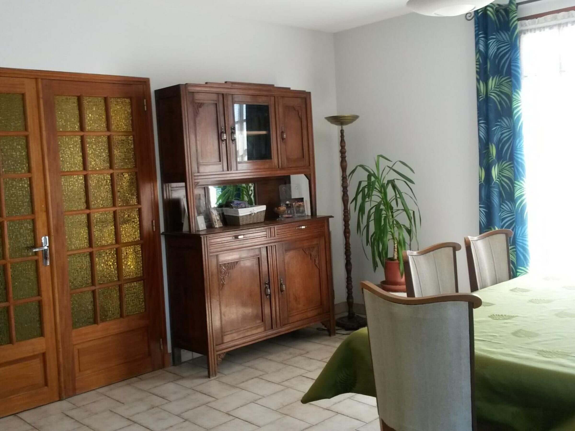 Une pièce comprenant un meuble en bois, une table à manger avec des chaises, une plante en pot et une lampe.