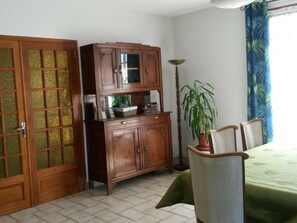 Una habitación con un armario de madera, una mesa de comedor con sillas, una planta en maceta y una lámpara.