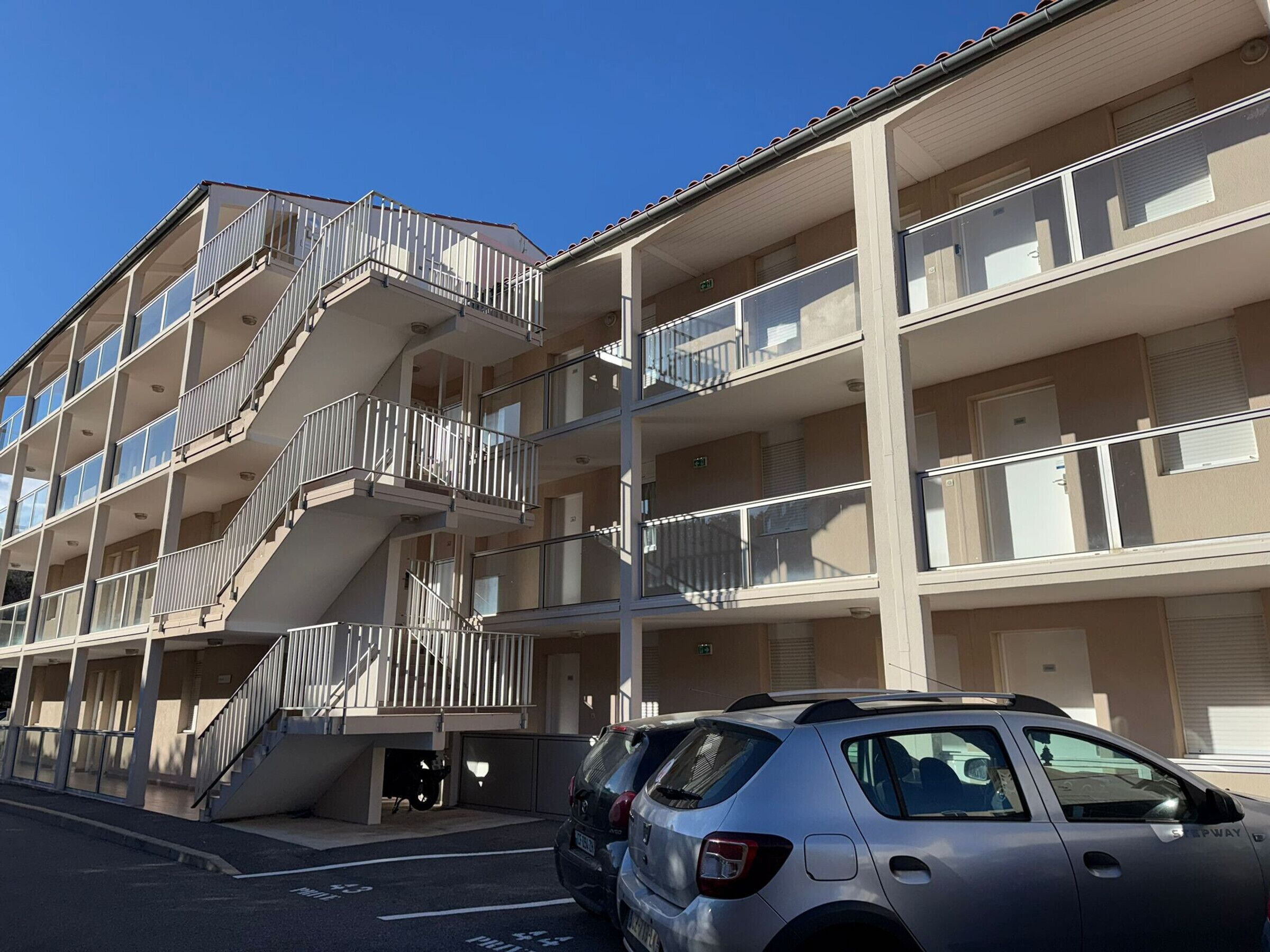 A multi-story building with balconies, a staircase, and a parked car.