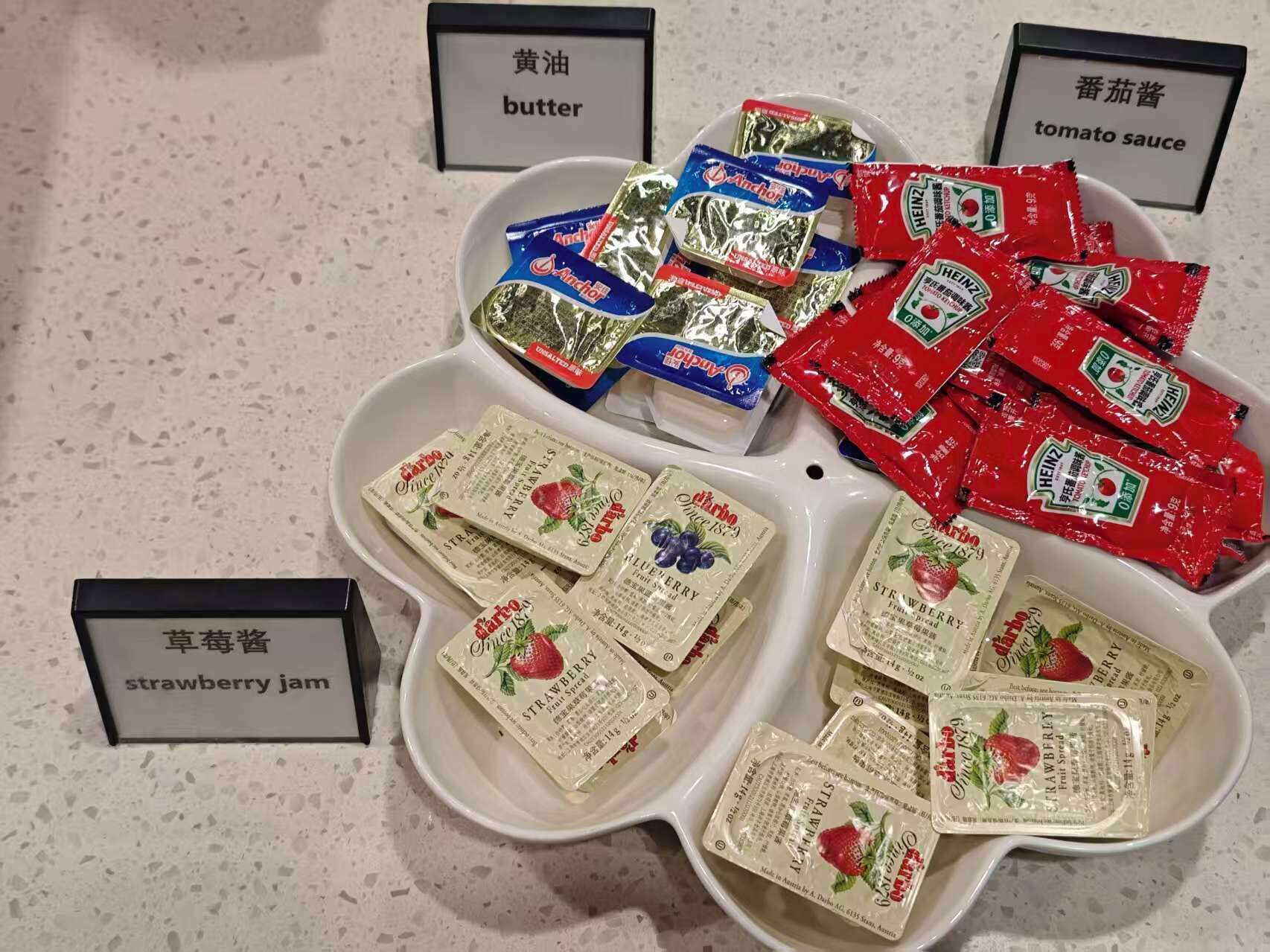 A table with labeled containers of food items including butter, tomato sauce, and strawberry jam.
