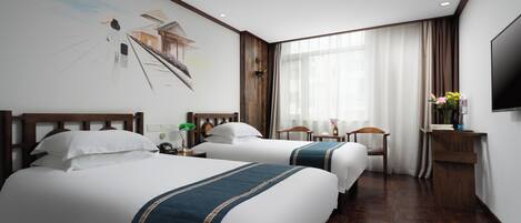 A hotel room with two beds, wooden headboards, a large window with curtains, a flat-screen TV, and a small desk with a lamp.