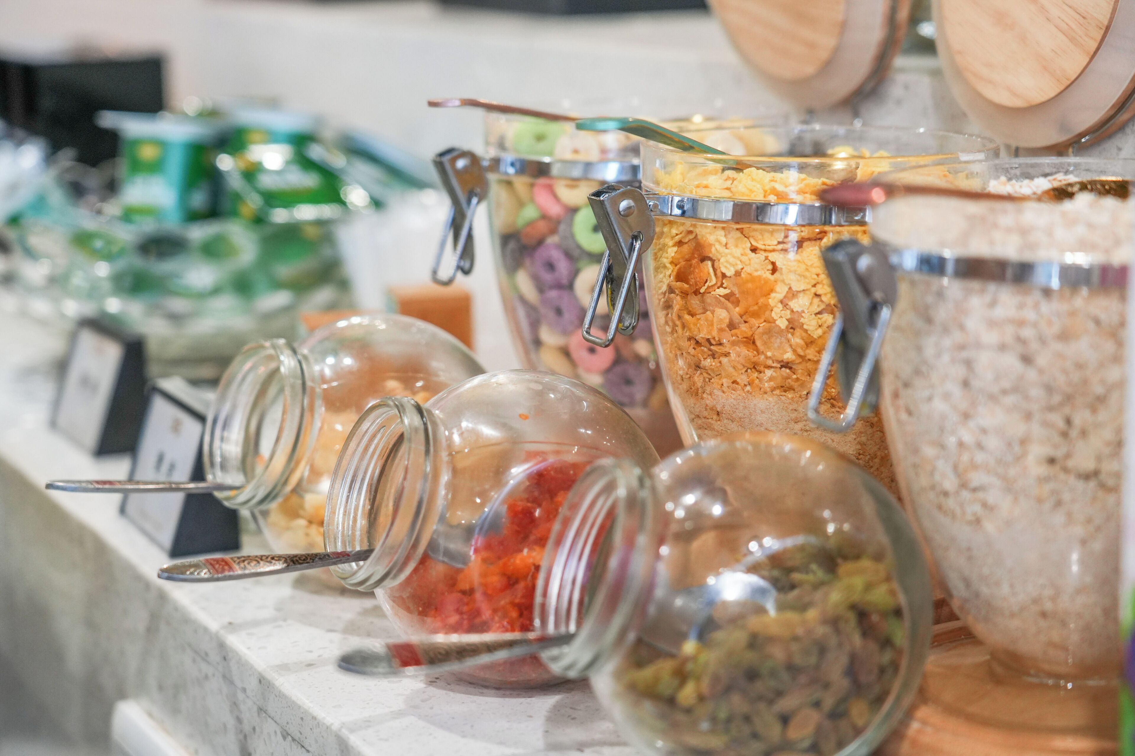 Un bufé con diversos alimentos en recipientes de vidrio, incluyendo cereales y untables.