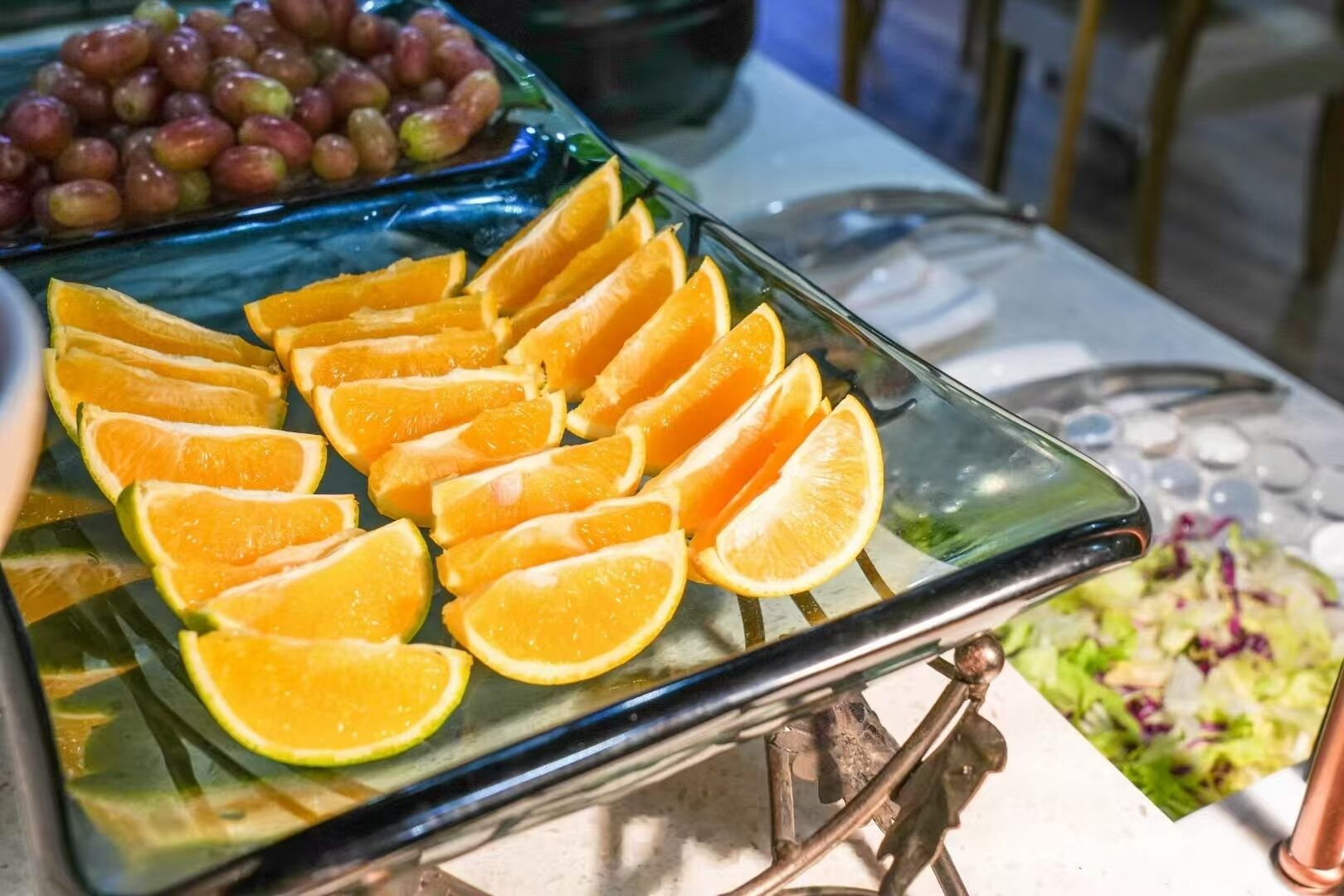 A buffet table with sliced oranges and grapes.
