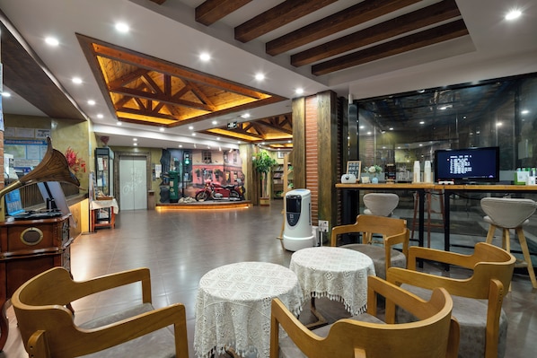 Un vestíbulo amplio con vigas de madera, un mostrador de recepción y una zona de estar con mesas y sillas redondas.