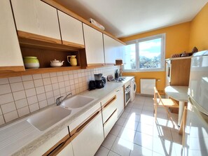 A modern kitchen with two sinks, a coffee maker, and a window with a view of trees.