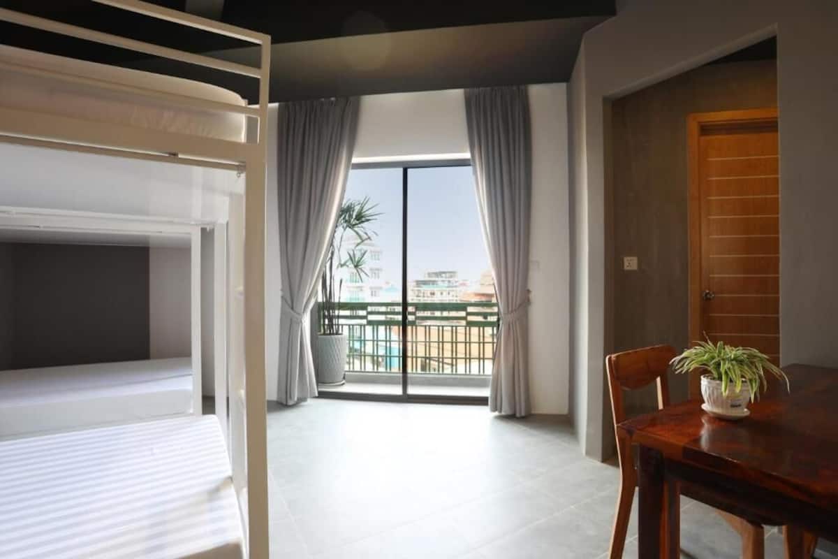 A room with a balcony, a dining table with a plant, and a wooden door.