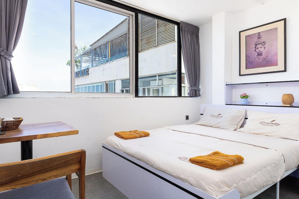 A bedroom with a bed, a table, a chair, and a window.