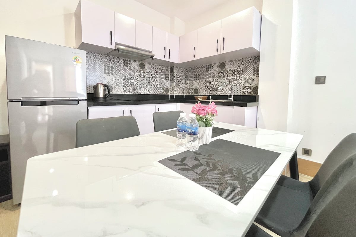A modern kitchen with white cabinets, a stainless steel refrigerator, a patterned backsplash, and a dining table with chairs.