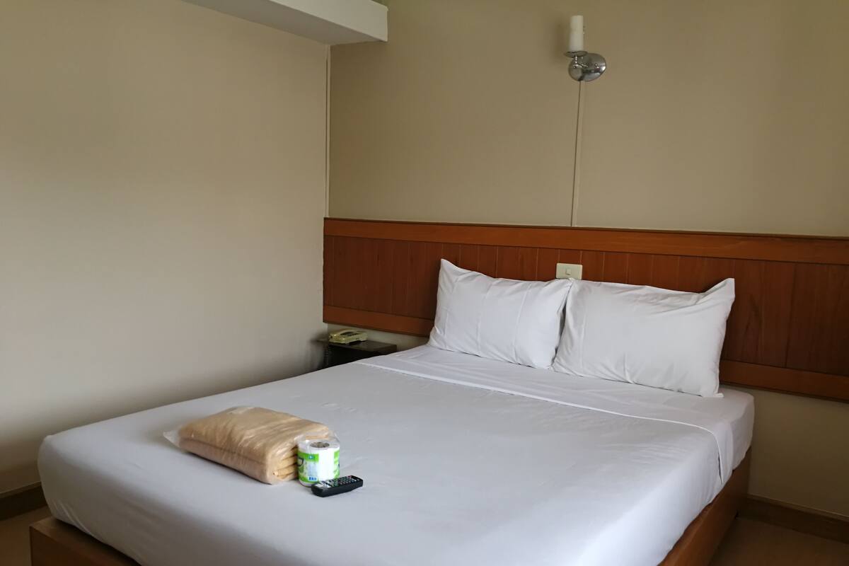 Cama bem arrumada com lençóis brancos, cabeceira de madeira e um controle remoto sobre a cama.