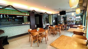 A restaurant with wooden tables and chairs, a tiled floor, and a counter with various items. - Srivichai Hotel (Nakhon Ratchasima)