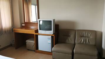 A hotel room with a wooden desk, a small refrigerator, a television, and a leather sofa.