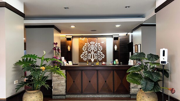 A reception area with a modern design, featuring a reception desk, decorative wall art, and potted plants. - Srivichai Hotel (Nakhon Ratchasima)