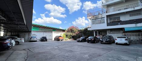 A parking area with several cars, a building with balconies, and a clear blue sky with clouds.