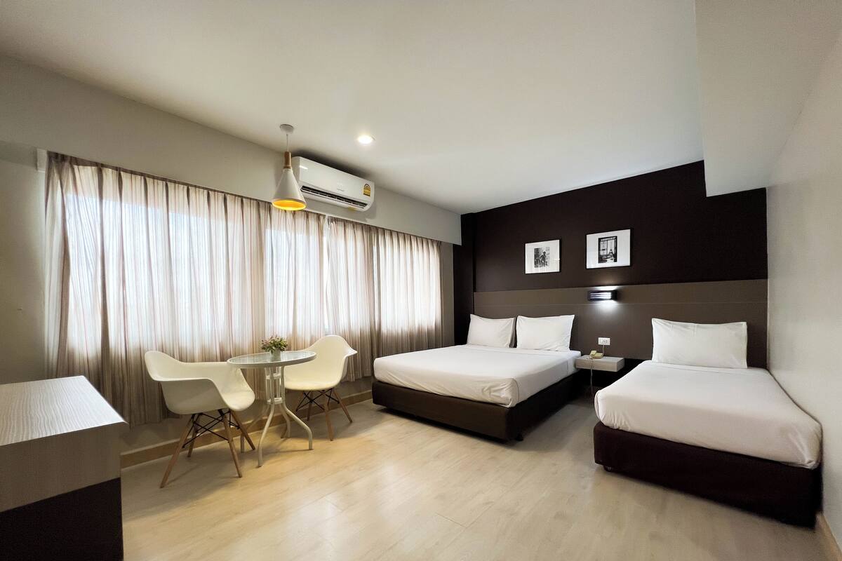 Quarto de hotel com cama, escrivaninha, cadeira e uma pequena mesa com um vaso.