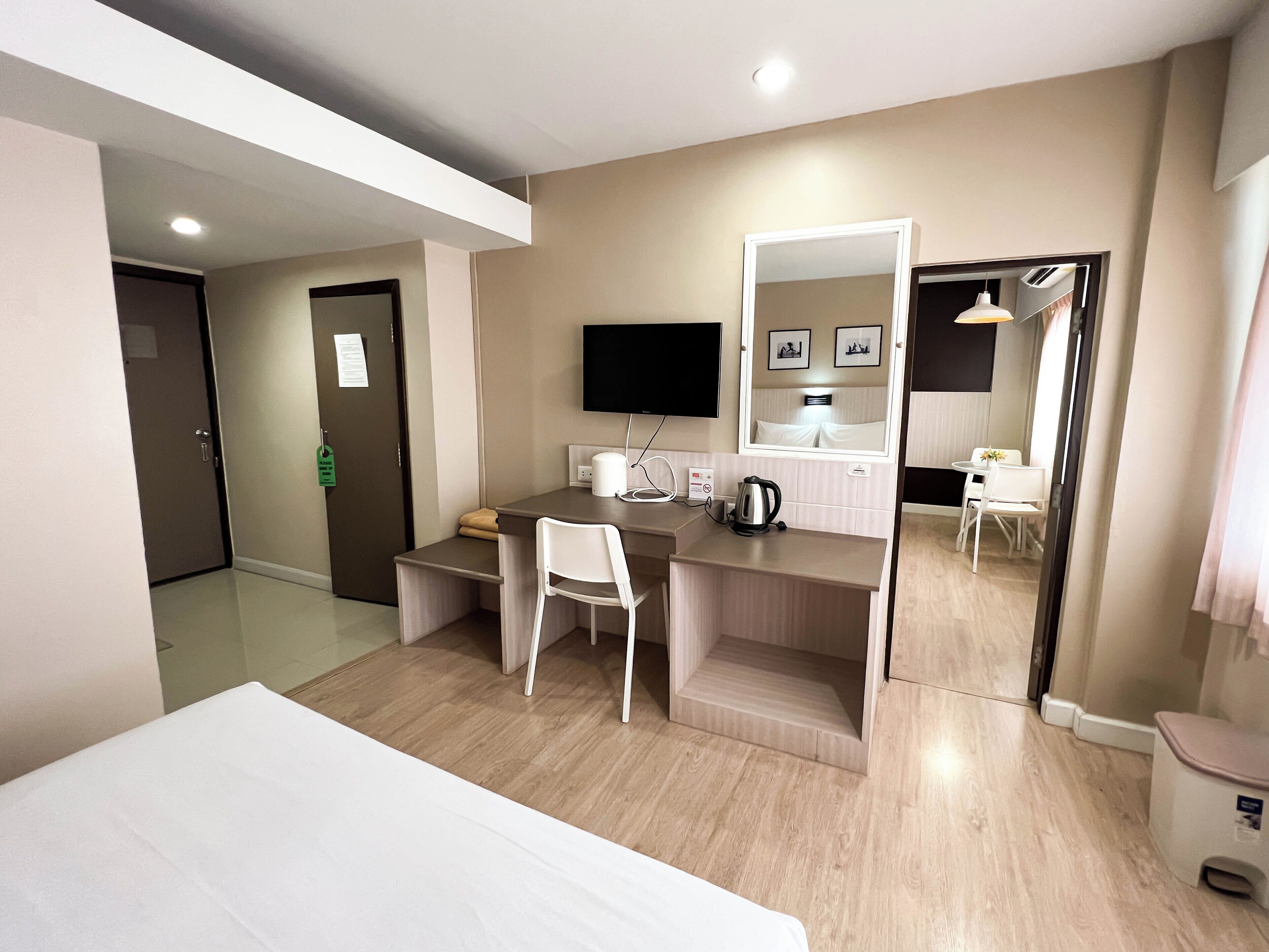 Habitación de hotel con cama, escritorio y silla, televisión, espejo y un pequeño comedor.