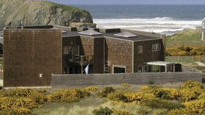 A modern building with a flat roof, large windows, and a view of the ocean. - Open 3100sf White Water View,  Pets Welcomed,  No Stair Entry (Bandon)