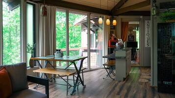 A modern kitchen with large windows, a dining area with a table and benches, and a visible kitchen counter.