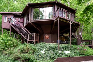 A multi-level wooden cabin with a sun dial, surrounded by dense greenery.