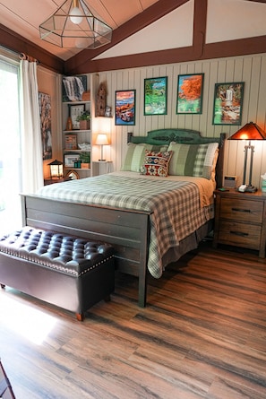 A bedroom with a bed, bedside tables, a bench, wall art, and a wooden floor.