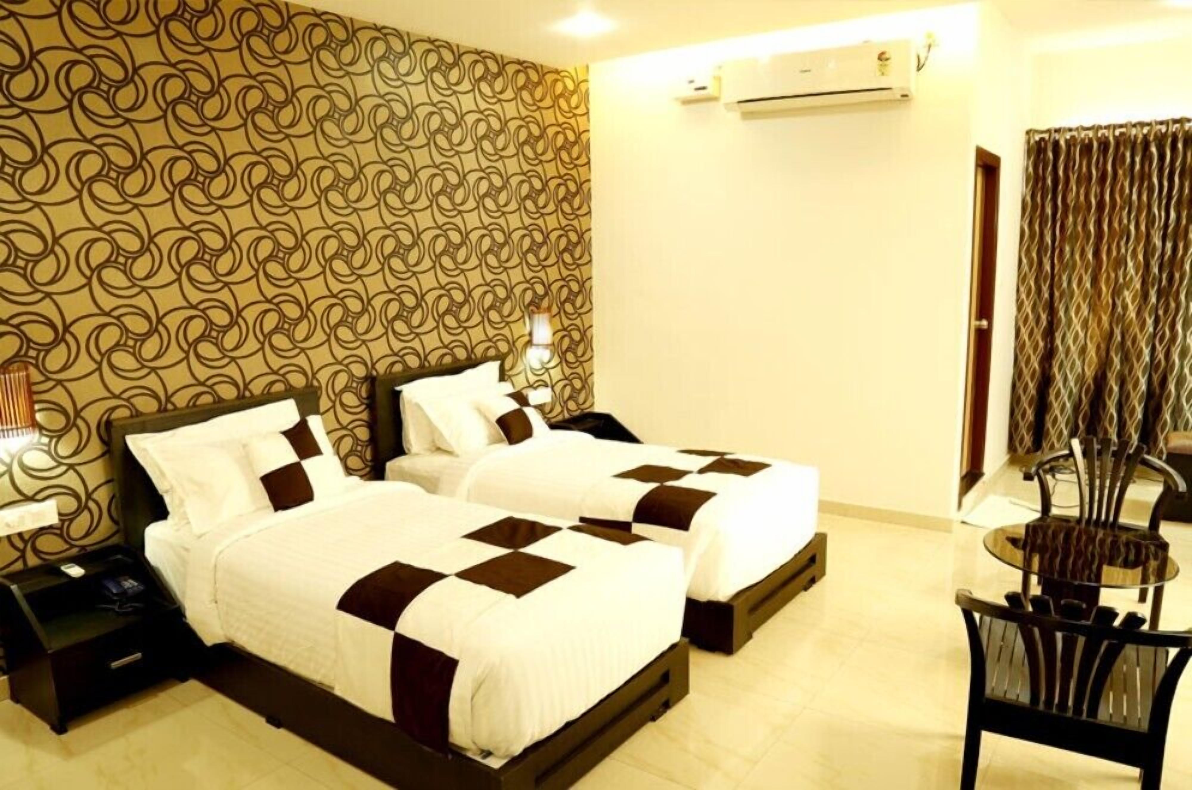 A hotel room with two beds, a small table, and a chair.