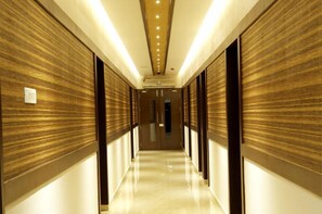 A long, narrow hallway with wooden paneling on the walls and a shiny floor, leading to a door at the end. - Rydges Inn (Tirur)