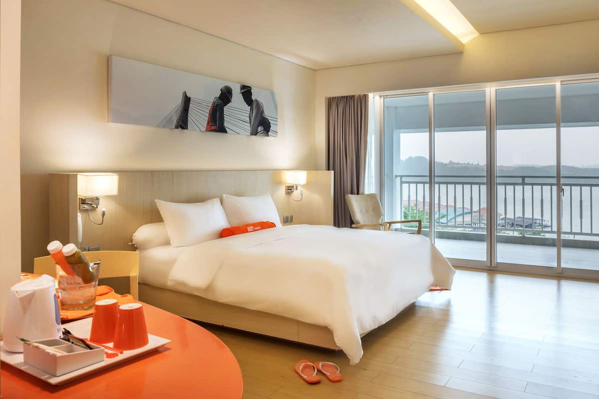 A hotel room with a large bed, a dining table with orange cups, a glass of water, and a pair of slippers on the floor.