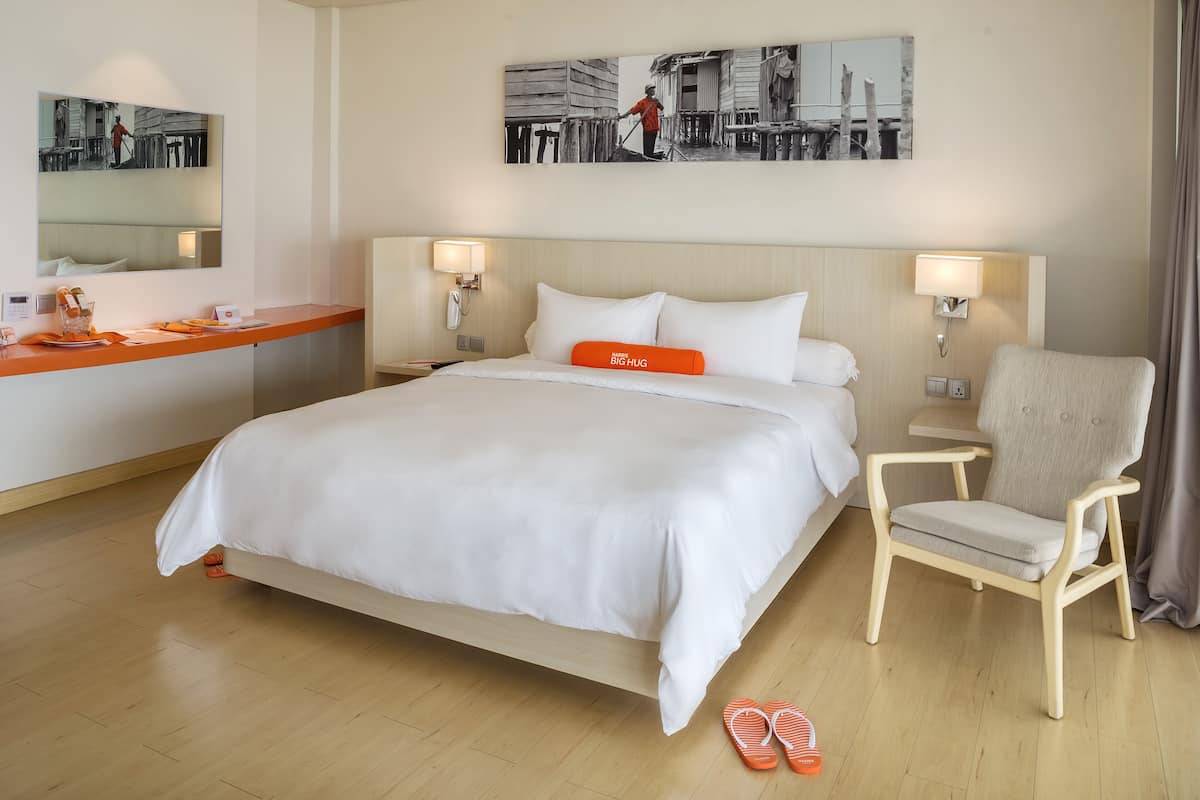 A hotel room with a bed, a chair, a desk, and a mirror.