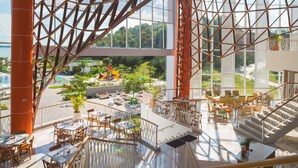 Amplio espacio interior con varias mesas y sillas para comer, una escalera y grandes ventanales que ofrecen vistas a una piscina y follaje.