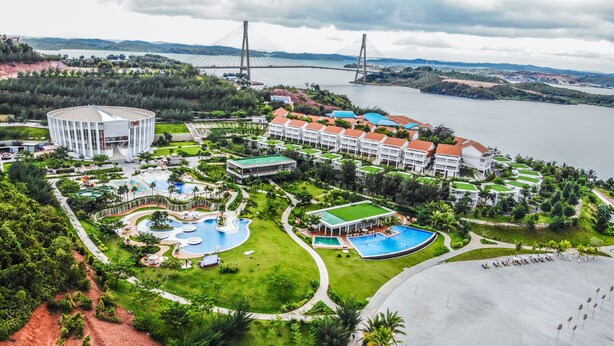 Un resort con varias piscinas, un edificio grande y un puente al fondo.