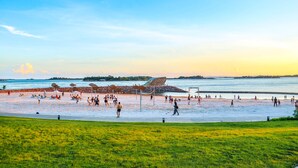Una playa con gente, una escultura grande y vistas al agua.