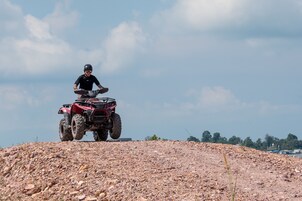 Eine Person fährt mit einem roten Quad über unwegsames Gelände.