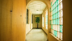 A hallway with a tiled floor, a wooden door on the left, and a window with green-tinted glass on the right. - The Stonehouse Hotel (Lekki)