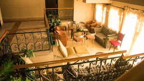 A spacious living area with a sofa set, armchairs, and a dining table. A staircase with a wrought iron railing is visible in the foreground. - The Stonehouse Hotel (Lekki)