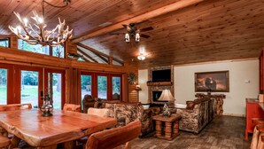 A rustic cabin interior with a wooden dining table, chairs, a sofa, and a fireplace. - Luxury Log Cabin in the Premier Resort-Holly Lake Ranch (Holly Lake Ranch)
