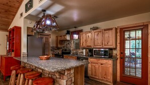 A kitchen with a granite island, wooden bar stools, a stone accent wall, and wooden cabinets. - Luxury Log Cabin in the Premier Resort-Holly Lake Ranch (Holly Lake Ranch)