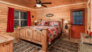 A wooden cabin bedroom with a bed, two bedside tables, a ceiling fan, and a door with a window. - Luxury Log Cabin in the Premier Resort-Holly Lake Ranch (Holly Lake Ranch)