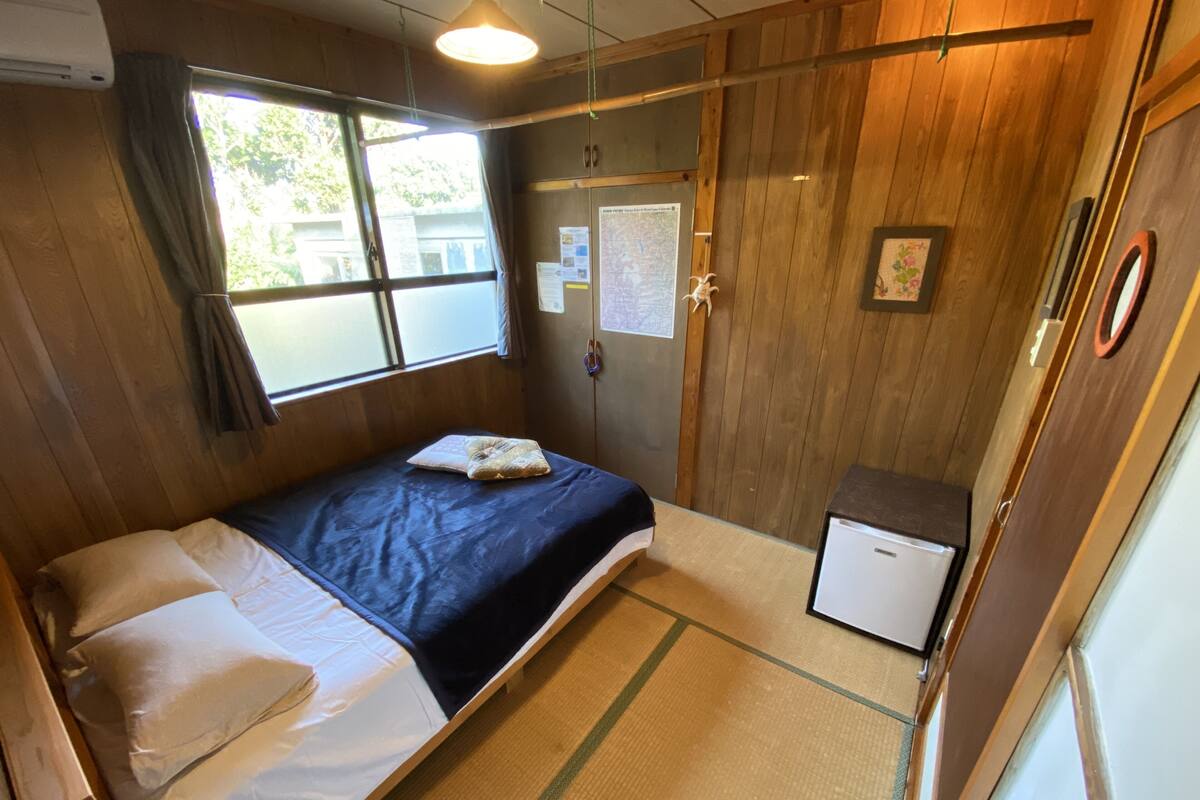 Una habitación compacta con una cama, un escritorio pequeño y un refrigerador.