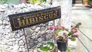 Une enseigne pour l’hôtel et le salon de beauté Hibiscus, avec un mur en pierre en arrière-plan et des plantes en pot.