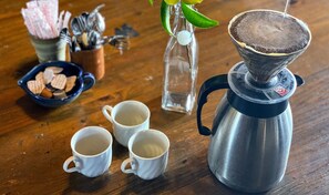 Une machine à café, deux tasses, un bol de biscuits et un verre d’eau sur une table en bois.