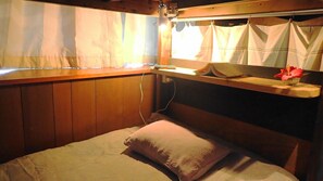 Une cabane avec un lit, une fenêtre avec des rideaux, une étagère avec des livres et une fleur, et un mur en bois.