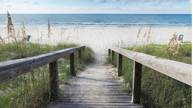 Un paseo marítimo de madera que conduce a una playa con vista despejada al océano.