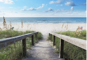 A wooden boardwalk leading to a beach with a clear view of the ocean.