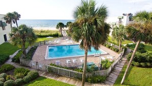 Una piscina rodeada de palmeras y una terraza de madera, con vistas a la playa y al océano.