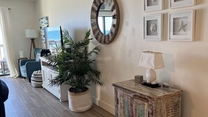 Una sala de estar con piso de madera, un espejo redondo, una planta en maceta, un mueble con paneles decorativos y obras de arte enmarcadas en la pared.