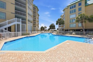 A swimming pool with a tiled deck, surrounded by multi-story buildings with balconies and palm trees.