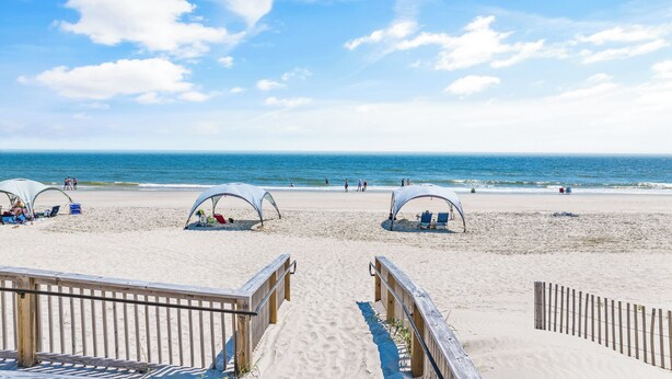 Une plage avec des passerelles en bois, des parasols et des chaises longues.